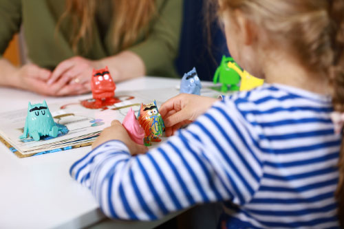Detailaufnahme einer Therapeutin während der Therapiestunde mit einem kleinen Mädchen, das mit Emotionsmonstern spielt