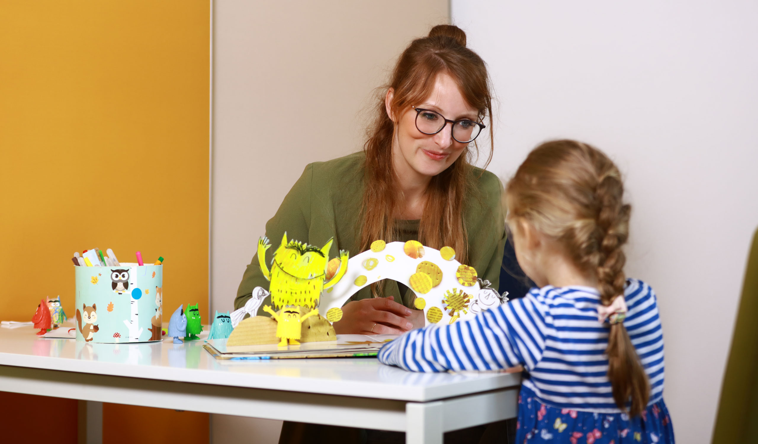 Therapeutin sitzt am Tisch mit jungem Mädchen während einer Therapiestunde